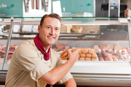 Portrait of happy butcher pointing at meat kept for selling in shopの写真素材
