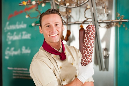 Smiling butcher showing fresh smoked sausage at his shopの写真素材