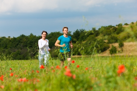 Young fitness couple doing sports outdoors; jogging on a green meadow in summer under a blue skyの写真素材