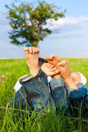 Happy couple lying on a meadow in summer, only feet to be seenの写真素材
