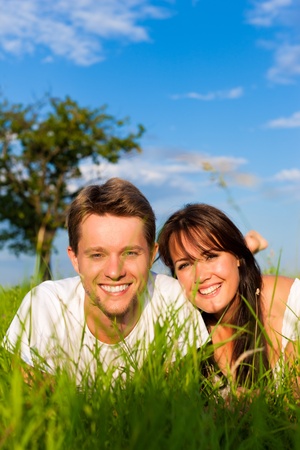 Happy couple lying on a meadow in summer, man and woman looking into the cameraの写真素材