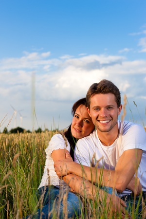 Happy couple sitting on a meadow or grainfield in summer embracing each otherの写真素材
