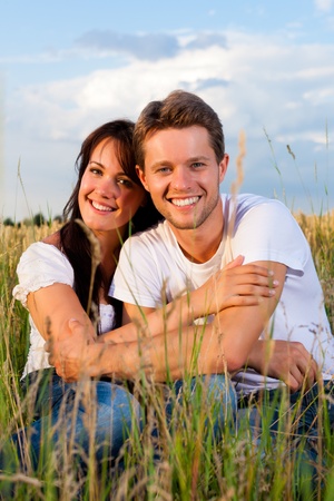 Happy couple sitting on a meadow or grainfield in summer embracing each otherの写真素材