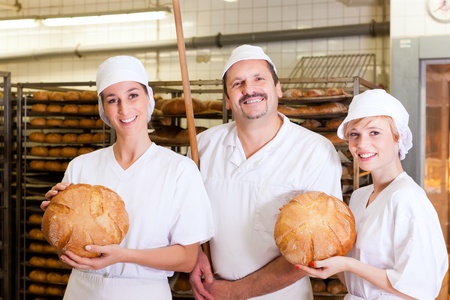 Baker standing with his team in bakery with freshly baked breadの写真素材