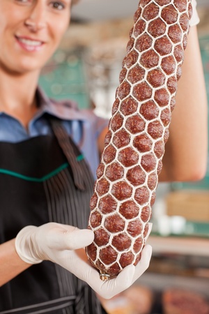 Smiling female butcher showing fresh sausage at butcheryの写真素材