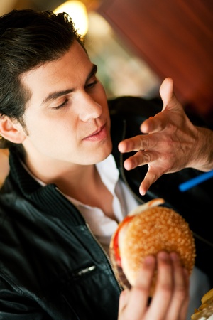 Man in a restaurant or diner eating a hamburger, he is hungry and having a good bite, shot with available light, very selective focusの写真素材