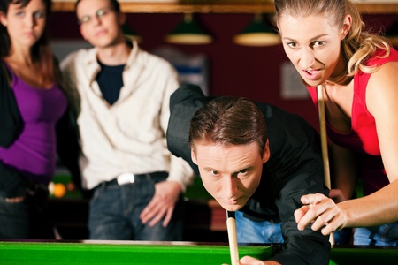Group of four friends in a billiard hall playing snooker