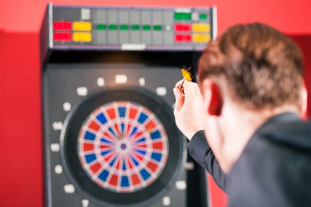Man playing darts aiming with the dart to hit the targetの写真素材