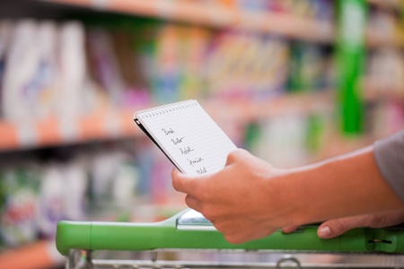 Female shopper holding checklist with trolley at supermarketの写真素材