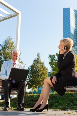 Business people working outdoors - he is working with laptop, she is calling someone on phoneの写真素材