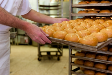 baker standing in his bakery in the morning and is baking bread or buns