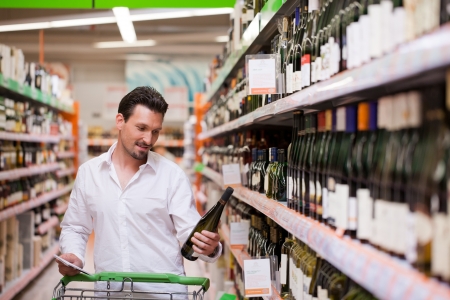Young man looking at bottle of wine in supermarketの写真素材