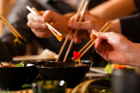 Young people eating in a Thai restaurant, they eating with chopsticks, close-up on hands and food Young people eating in a Thai restaurant, they eating with chopsticks, close-up on hands and food