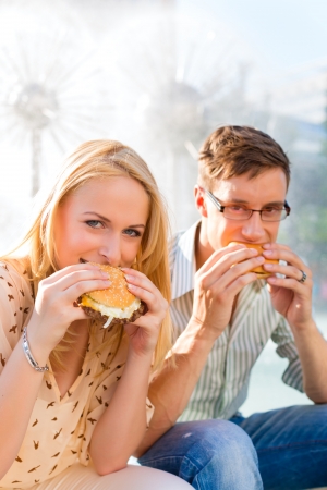 Couple is hungry and eats a burger at lunch time in the sunの写真素材