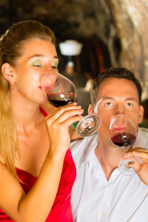 Couple - man and woman- tasting red wine in a cellar, in the background barrels can be seenの写真素材