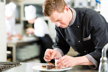 Cook, the pastry chef, in hotel or restaurant kitchen cooking, he is finishing a sweet dessert Cook, the pastry chef, in hotel or restaurant kitchen cooking, he is finishing a sweet dessert