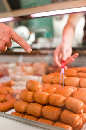 Cropped image of customer pointing with butcher holding fork at meat counterの写真素材