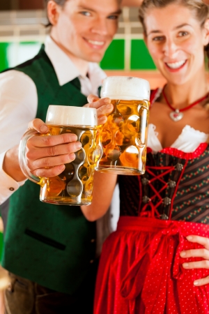Young man and woman in traditonal Tracht with beer glass in brewery, in front of brewing kettleの写真素材