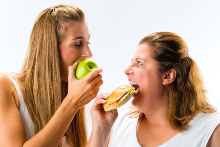 Healthy against unhealthy - Thin and fat woman eating an apple and sandwichの写真素材