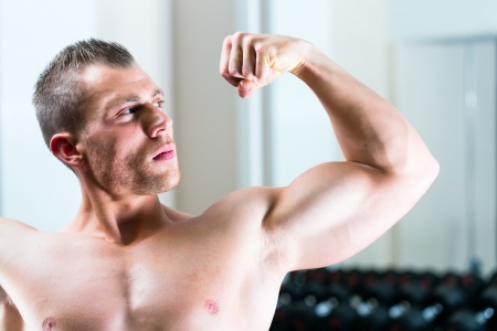 Strong man, bodybuilder posing in Gym, dumbbells are in the backgroundの写真素材