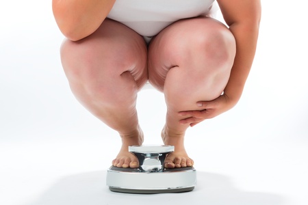 Diet and weight, obese young woman crouching on a scale measuring her weight