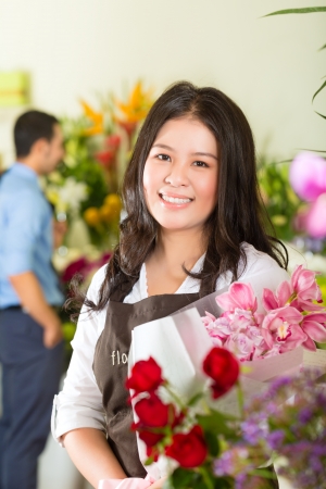 Friendly Asian florist or Saleswoman in a flower shop, holding a flower bouquet, in the background is a customerの写真素材