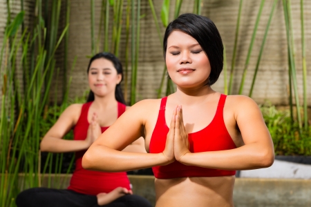 young Asian women sitting in yoga position while meditating in tropical settingの写真素材