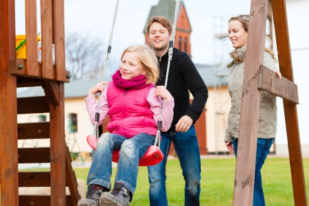 Girl sitting on a swing, father on mother pushingの写真素材