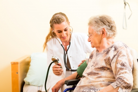 Young nurse and female senior in nursing home, the blood pressure is going to be measuredの写真素材