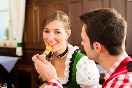 Young couple in traditional Bavarian Tracht eating in restaurant or pub lunch or dinnerの写真素材