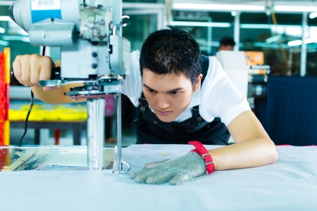 worker using a cutter - a large machine for cutting fabrics- in a Chinese textile factory, he wears a chain glove worker using a cutter - a large machine for cutting fabrics- in a Chinese textile factory, he wears a chain glove
