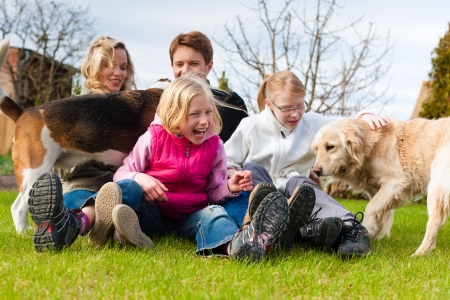 Family, father, mother and daughters, sitting together with their dogs on a meadow, they laugh and have funの写真素材