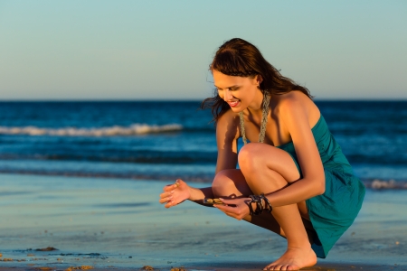 Woman looking for shells at the ocean beach in sunsetの写真素材