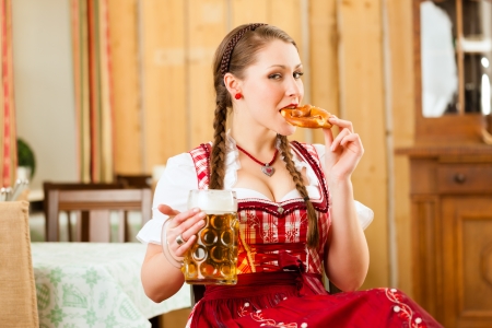 Young woman in traditional Bavarian Tracht in restaurant or pub with beer and steins and pretzelの写真素材