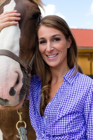Young woman in the stable with horse in sunshine and smilingの写真素材