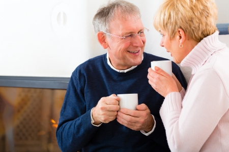 Seniors at home in front of fireplace with tea cupの写真素材