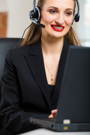 Young businesswoman or secretary working in her Office, she sitting in front of the window and working on a computer with a headset, she has a customer pitchの写真素材