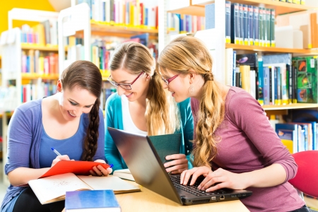 Students - Young women in library with laptop and book learning in groupの写真素材