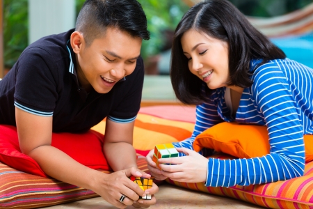 Young Indonesian couple - man and woman - at home playing with a magic cubeの写真素材