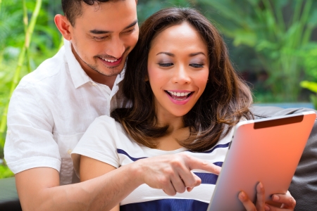 Young Indonesian couple - man and woman - sitting with a tablet computer on a couchの写真素材