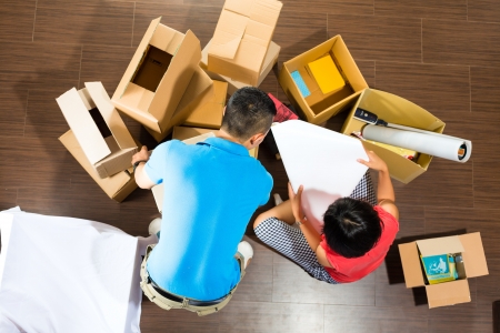 Real estate market - Young Indonesian couple moving in a home or apartment, they unpacking moving boxesの写真素材