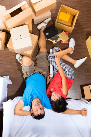 Real estate market - Young Indonesian couple moving in a home or apartment, they unpacking moving boxesの写真素材