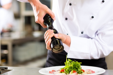 Chef in hotel or restaurant kitchen cooking, only hands to be seen, he is seasoning dishesの写真素材