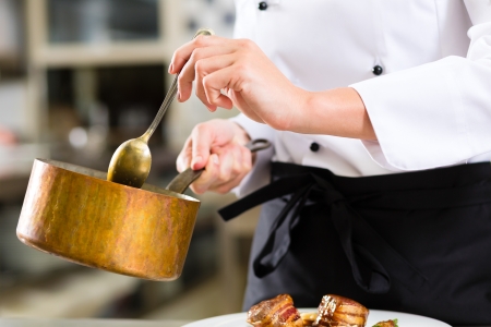Female Chef in hotel or restaurant kitchen cooking, only hands to be seen, she is working on the sauce as saucierの写真素材
