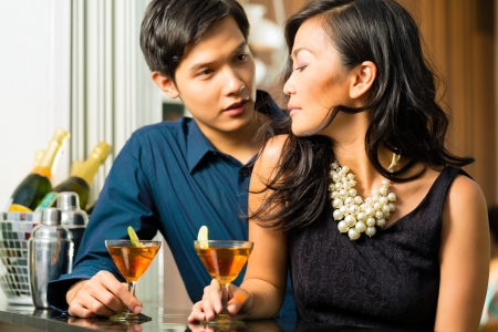 Asian man and woman in flirting intimately at bar drinking cocktailsの写真素材