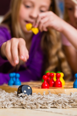 Family - two sisters - playing board game ludo at home on the floor, focus on dice in the frontの写真素材