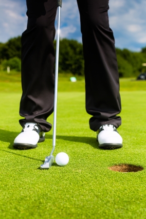 Golf player putting ball into hole, only feet and iron to be seenの写真素材