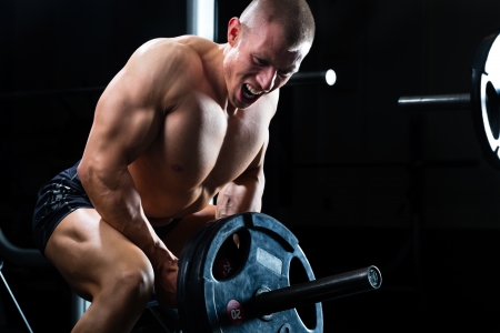 Strong man - bodybuilder with dumbbells in a gym, exercising with a barbell