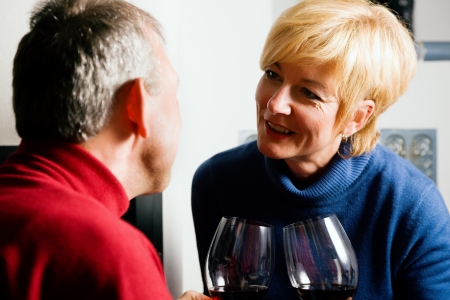 Mature couple having fun clinking glasses with red wine in a romantic settingの写真素材
