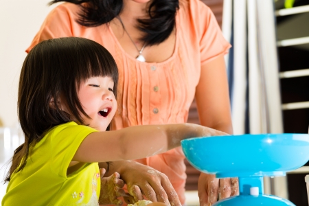 Indonesian Asian Little girl and her mother in the kitchen bake a cake togetherの写真素材